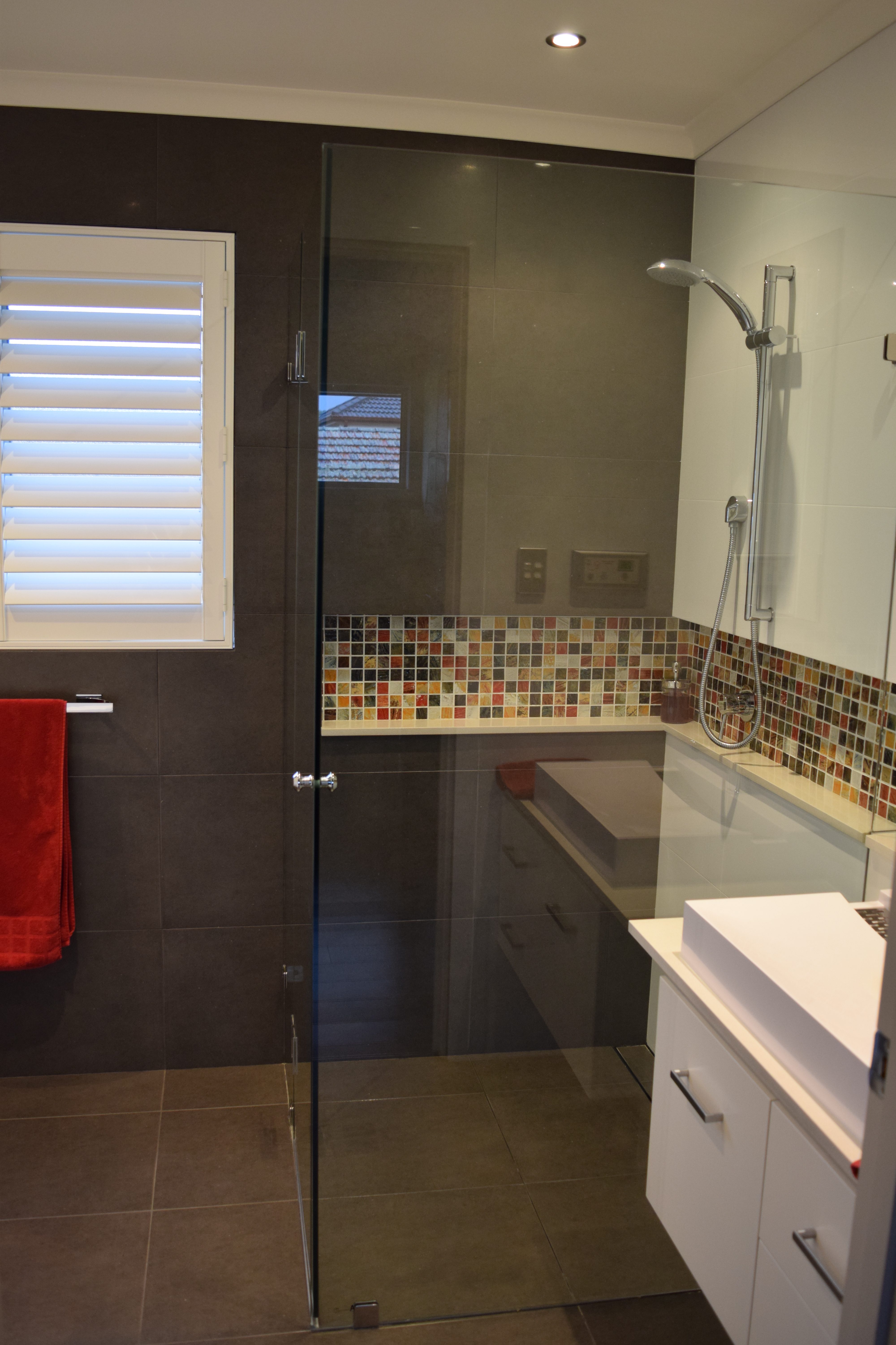 Modern bathroom with white basin and shower niche containing colourful mosaic tiles